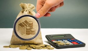 Person pins a coin bag closed beside a calculator, suggesting saving and budgeting