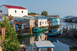 Colorful stilt houses along a calm waterfront with boats tied to docks under a clear blue sky far edge of the coast.