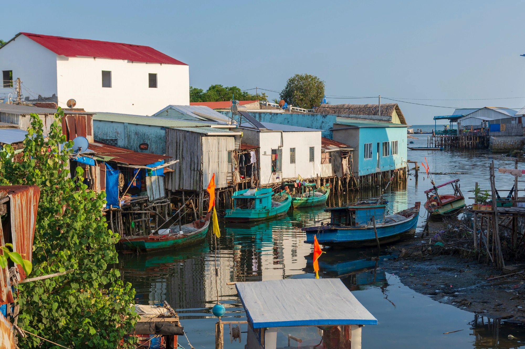 Colorful stilt houses along a calm waterfront with boats tied to docks under a clear blue sky far edge of the coast.