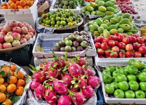 Colorful market fruit stand with crates of dragon fruit, green apples, red apples, oranges, and mangoes on display.