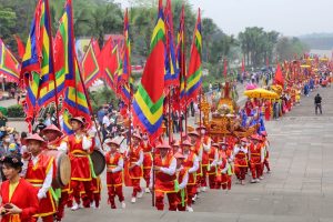 Vibrant parade with flag-bearers in red and gold costumes carrying colorful, striped flags down a wide street.