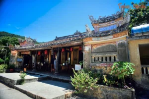 Traditional Asian temple with ornate curved roofs, red lanterns, and stone walls on a sunny day.
