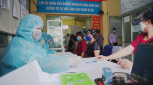 Healthcare workers in full PPE at a clinic desk assisting patients wearing masks.