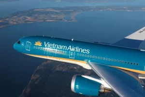 Vietnam Airlines plane in turquoise livery flying above a coastline and water, engine visible beneath the wing