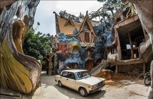 Whimsical fantasy house with carved rock walls and colorful turrets, a vintage beige car parked in front.