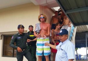 Shirtless men on stairs being guided by uniformed security guards outside a building.