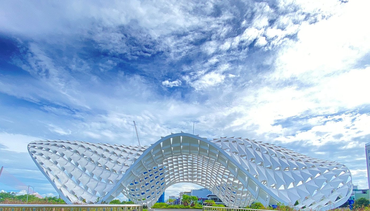 Futuristic white lattice arch building with wing-like curved sections under a bright blue sky.