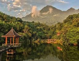 Scenic lake with a wooden pavilion on the left, surrounded by trees and distant mountains in the background.