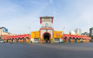 Historic gateway of Ben Thanh Market with colorful festival arches and Vietnamese flags in Ho Chi Minh City.