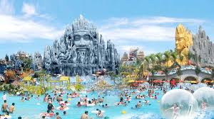 Crowded water park featuring towering stone-carved faces and colorful slides under a blue sky.