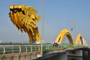 Yellow dragon sculptures arch over a bridge, with green railing and clear blue sky in the background.