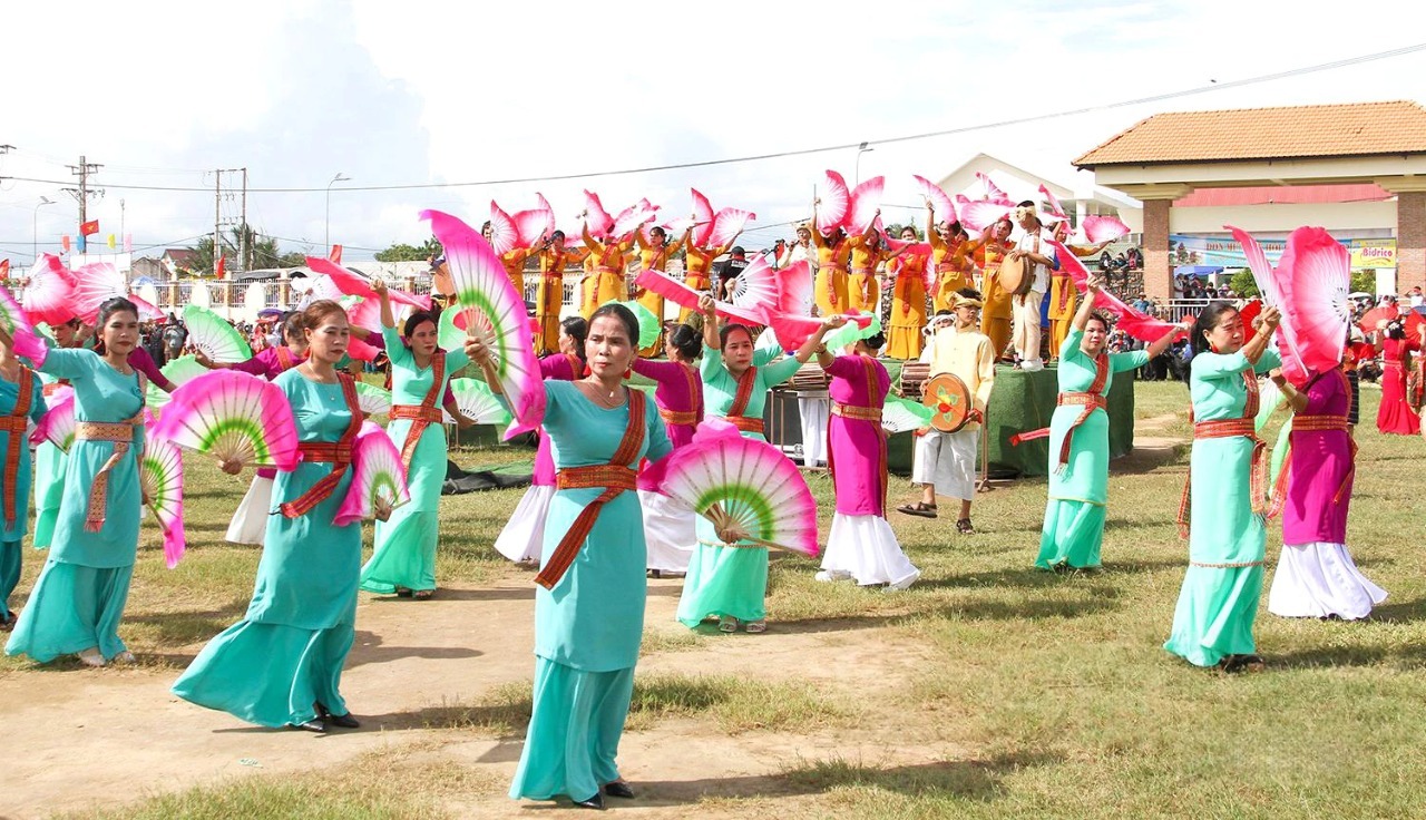 Group of women in turquoise dresses performing a fan dance on a grassy field during a festival.