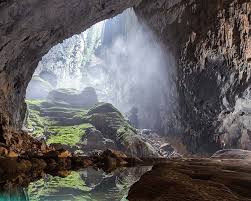 Cave interior with a waterfall cascading into a calm pool and mossy rocks nearby.