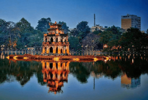 Three-story brick pagoda on a small island in a calm lake, its orange reflections shimmering in the water.