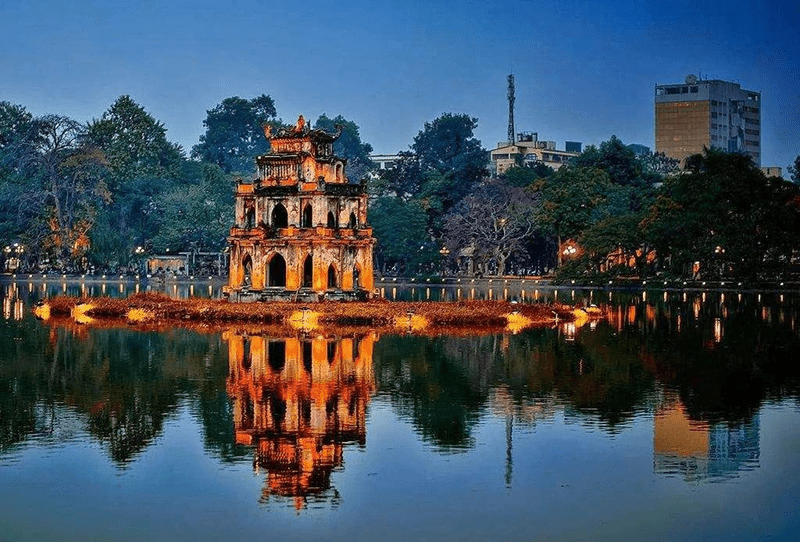 Three-story brick pagoda on a small island in a calm lake, its orange reflections shimmering in the water.