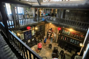 Two-level wooden interior with visitors exploring a museum-like room, red lanterns hanging, and wall displays.