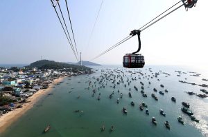 Aerial view of a seaside town as a cable car passes over a crowded harbor of small boats.