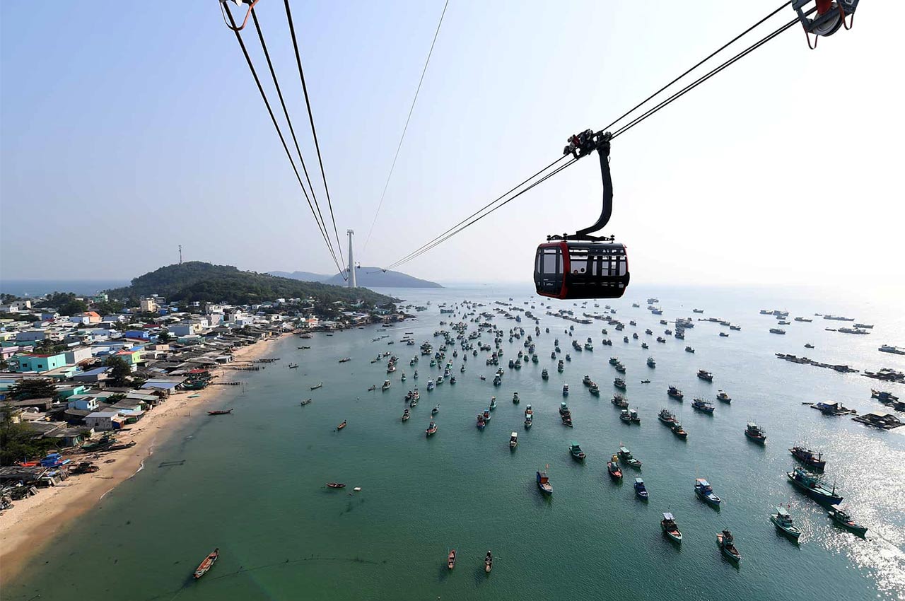 Aerial view of a seaside town as a cable car passes over a crowded harbor of small boats.