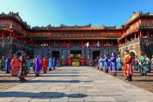 Colorfully dressed performers stand in two lines in a historic Chinese palace courtyard during a ceremonial event.