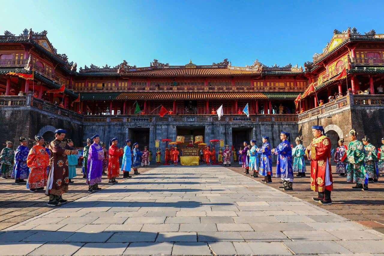 Colorfully dressed performers stand in two lines in a historic Chinese palace courtyard during a ceremonial event.