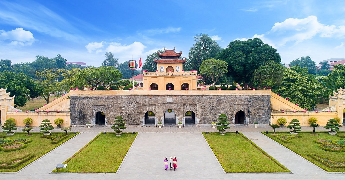 Historic stone fortress with arched doorways and a yellow pavilion on top, set in a manicured garden with trees nearby.