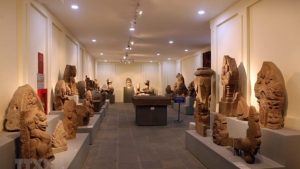 Interior of a museum gallery with numerous stone sculptures on pedestals along beige walls and a central display case.
