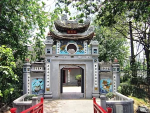 Ornate Chinese temple gate with dragon motifs, circular moon gate, and blue ceramic panels framed by greenery.