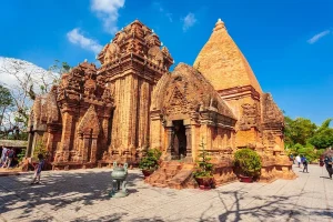 Ancient red-brick temple with a tall conical tower in a sunny courtyard; visitors walk nearby.