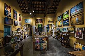 Interior of a warm-toned art gallery with framed paintings on all walls and display pedestals in the center.