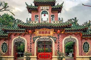 Ornate Chinese temple gate with green tiled roofs, pink brick walls, red lanterns, and intricate carvings.
