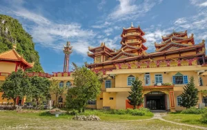 Vibrant temple complex with a multi-tiered pagoda, red-gold roofs, yellow walls, and green trees under a blue sky.