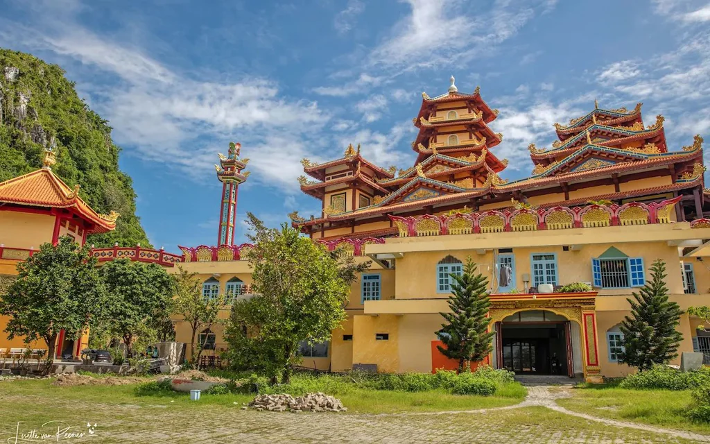 Vibrant temple complex with a multi-tiered pagoda, red-gold roofs, yellow walls, and green trees under a blue sky.