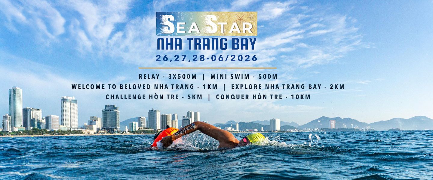 Swimmer in open water with a blue city skyline in the background and an event banner overhead reading Sea Star Nha Trang Bay 2026 (June 26–28).