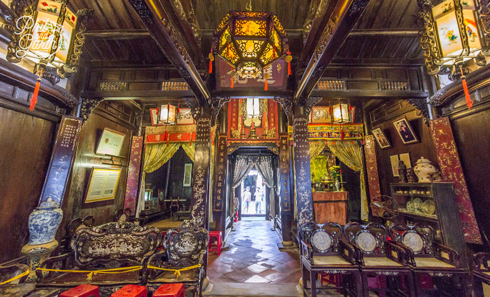 Intricately carved wooden interior of a Chinese hall with hanging lanterns, antique furniture, and an altar at the far end leading to a courtyard.