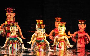 Colorful traditional puppets with crowns arranged in shallow water on a dark stage, prepared for a performance.