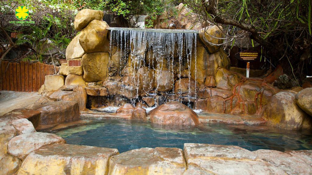 Rock waterfall cascading into a turquoise pool, surrounded by large stones in a garden setting.