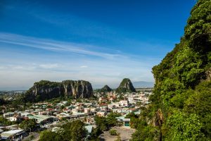 Town nestled at the foot of limestone hills with a bright blue sky and green cliffs on the right.