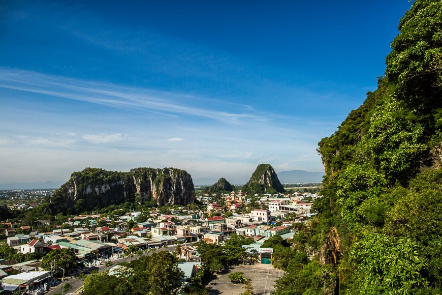 Town nestled at the foot of limestone hills with a bright blue sky and green cliffs on the right.