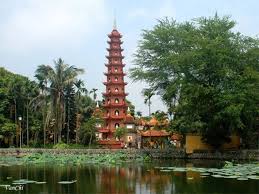 Red, multi-tiered pagoda beside a pond with lotus leaves, framed by palm trees and lush greenery.