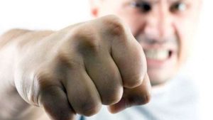 Close-up of a clenched fist reaching toward the viewer, with an angry, blurred man in the background.