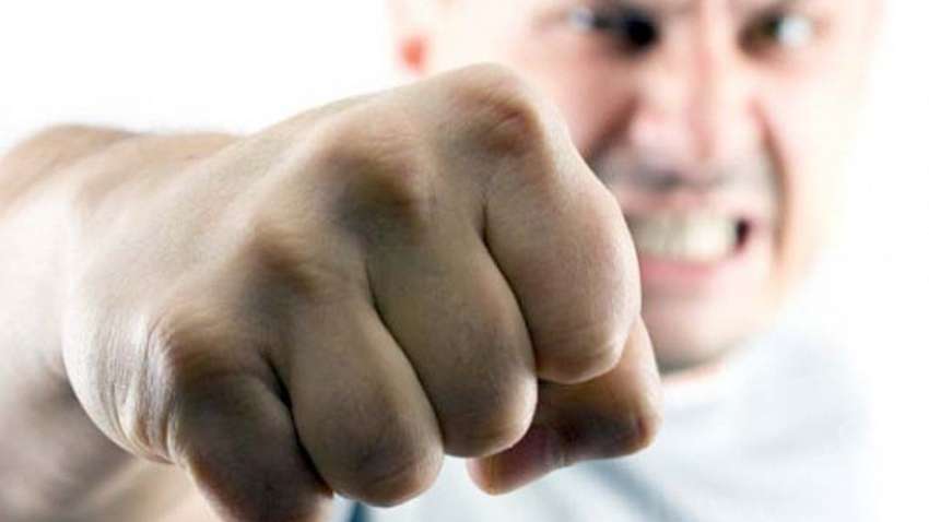 Close-up of a clenched fist reaching toward the viewer, with an angry, blurred man in the background.