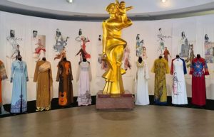 Gold sculpture of a family centerpiece surrounded by mannequins wearing colorful áo dài dresses in a museum-like exhibit