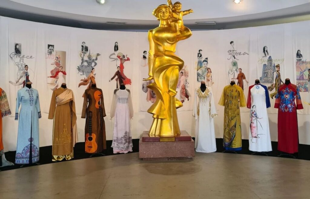 Gold sculpture of a family centerpiece surrounded by mannequins wearing colorful áo dài dresses in a museum-like exhibit