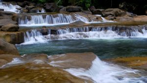 Tiered waterfall flowing over smooth brown rocks into a turquoise pool