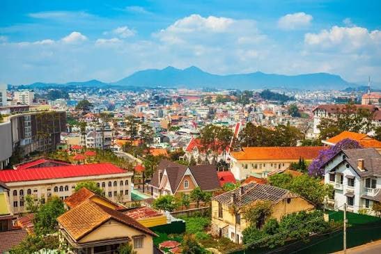 Colorful hillside town with clustered houses and red-tiled roofs, mountains in the distance under a blue sky.