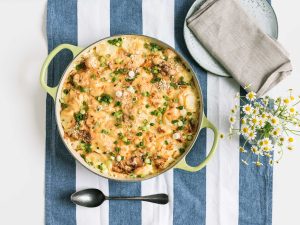 Cheesy potato bake with mushrooms and chopped green onions in a lime-green pan on a blue-and-white striped tablecloth.
