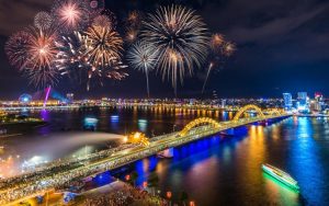 Night panorama of the Han River in Da Nang, Vietnam, with fireworks, city lights and a bridge over the river.