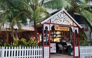 Small open-air cafe with a white picket fence and ornate red-and-white pavilion amid palm trees.